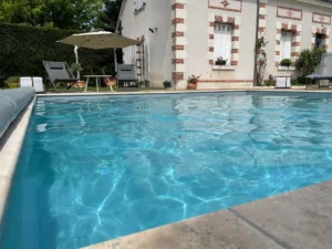Piscine extérieure devant maison avec transats et parasol